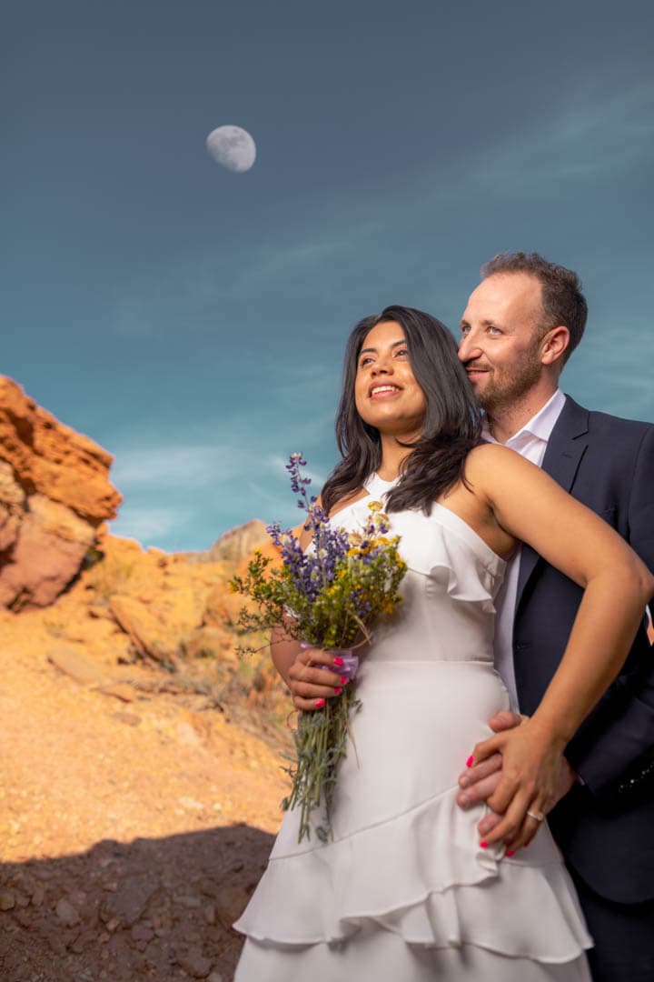 A bride and groom posing in front of the moon.