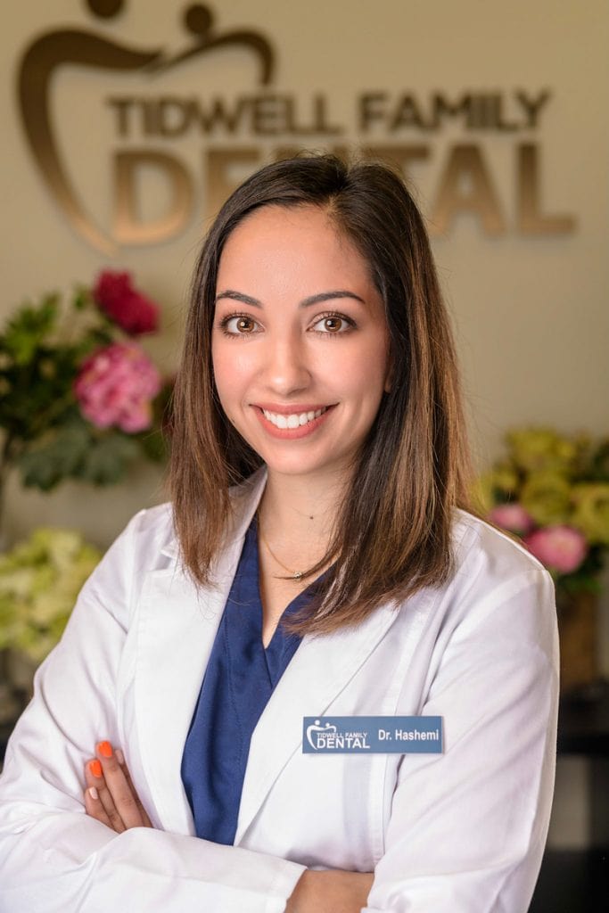 Woman Dentist headshot with long hair and big eyes in front of logo