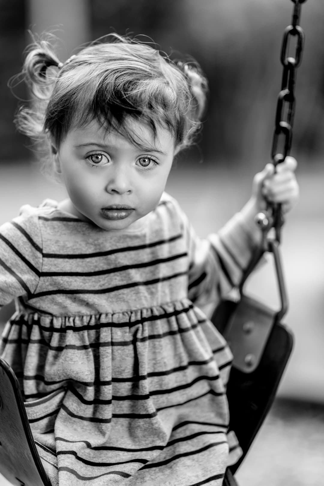 A black and white photo of a little girl on a swing.