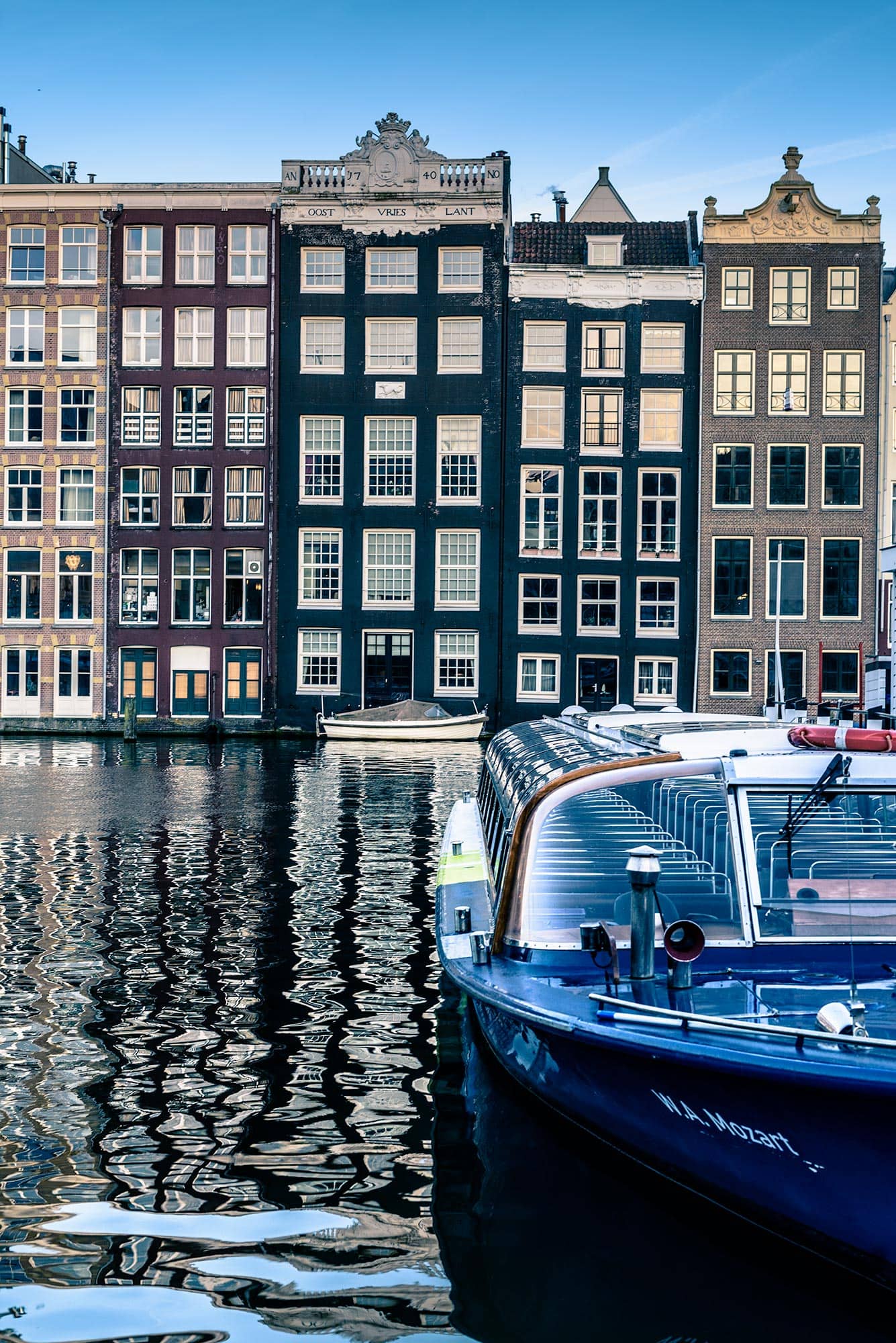 A blue boat is docked in front of a row of buildings.