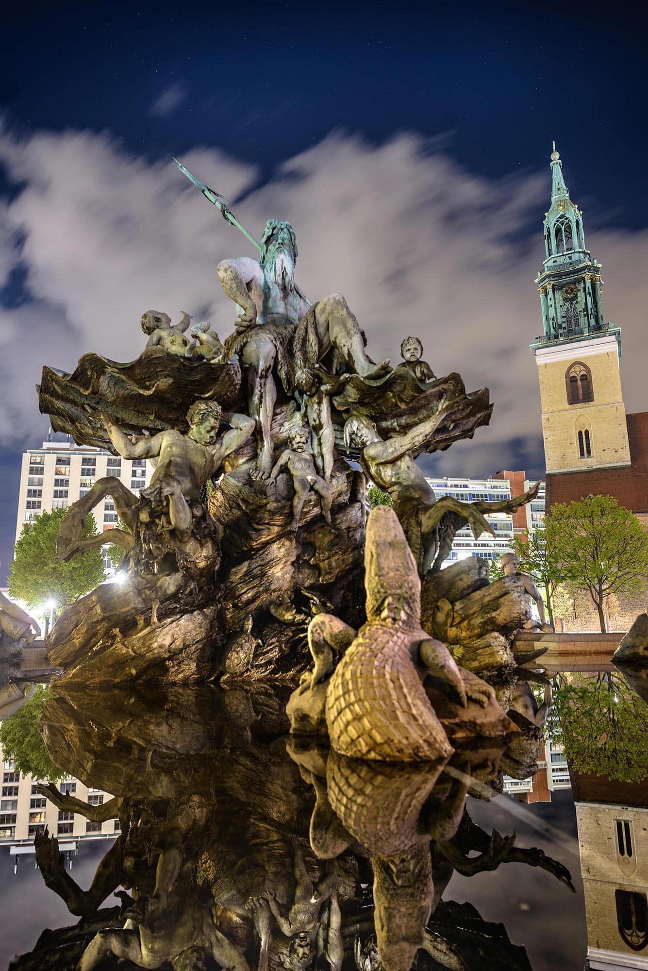 A fountain with statues and a clock tower in the background.