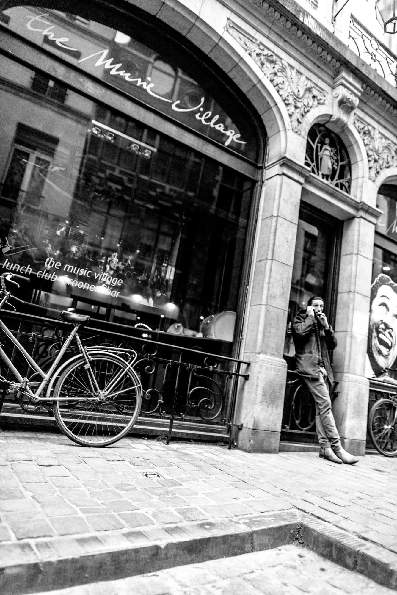 A black and white photo of a man with a bicycle in front of a building.