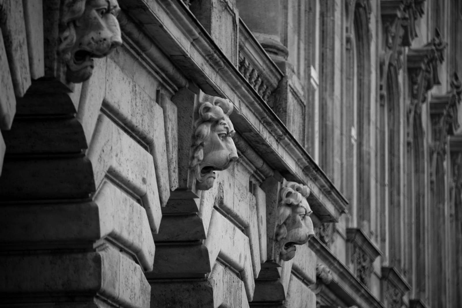 Black and white photo of lion heads on the side of a building.