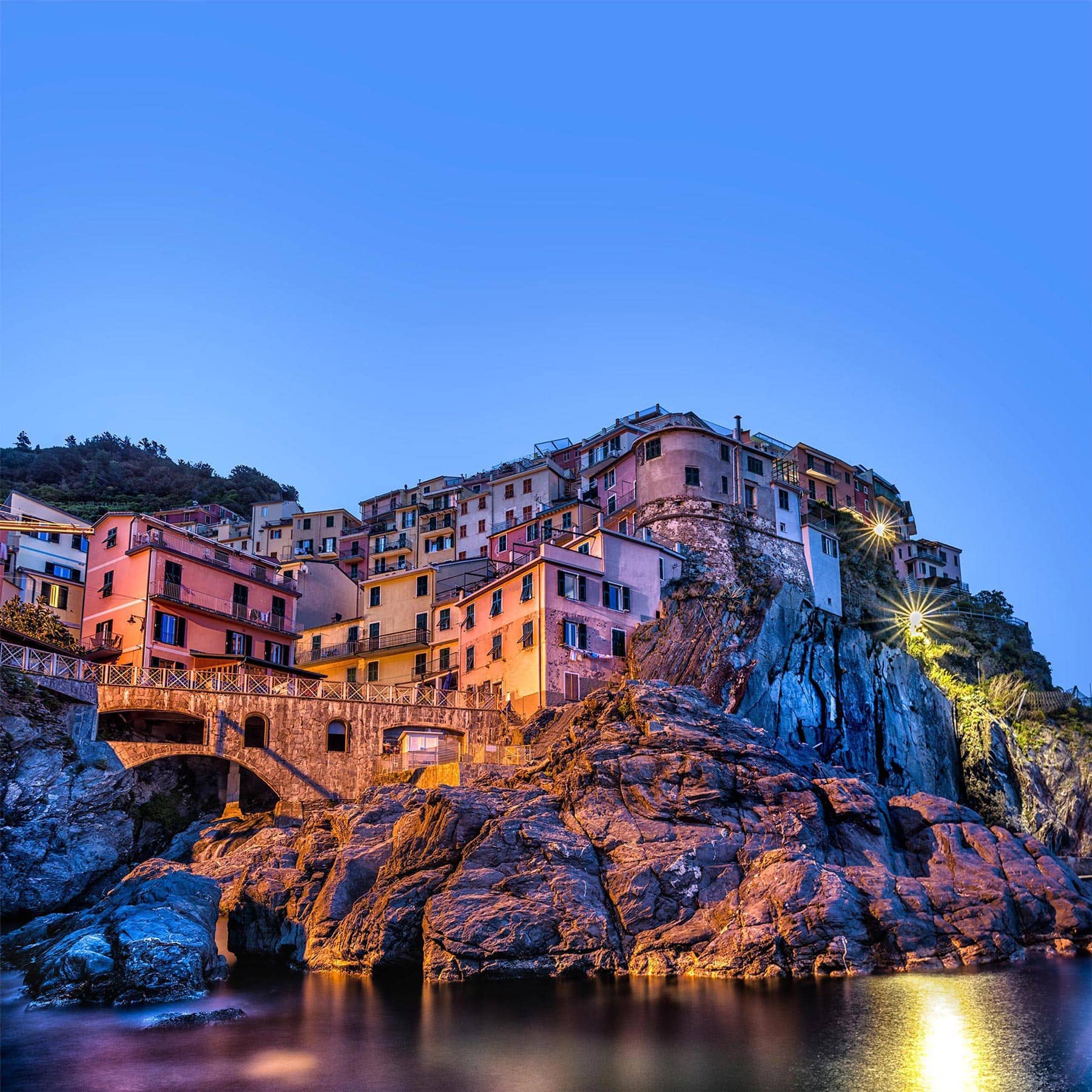 A colorful village sits on top of a cliff overlooking the ocean.