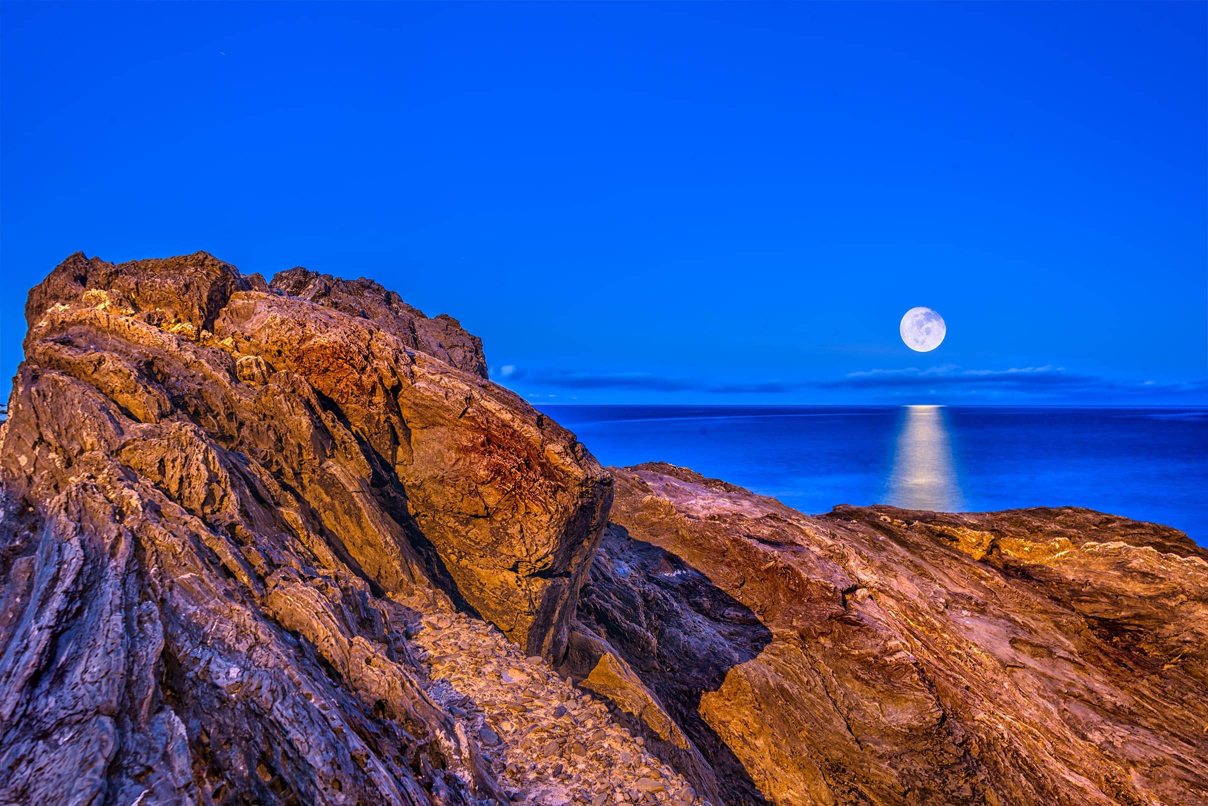 A full moon rises over a rocky cliff.