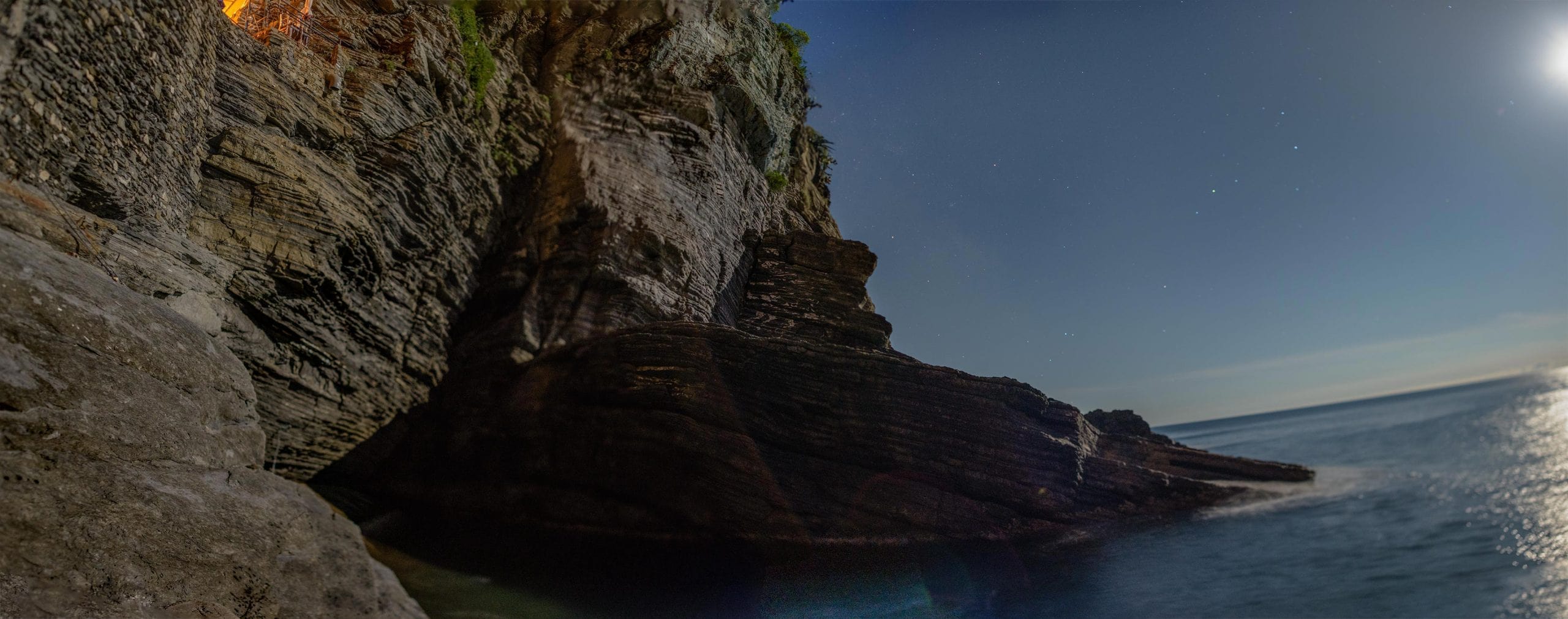 A rocky cliff with a full moon above it.