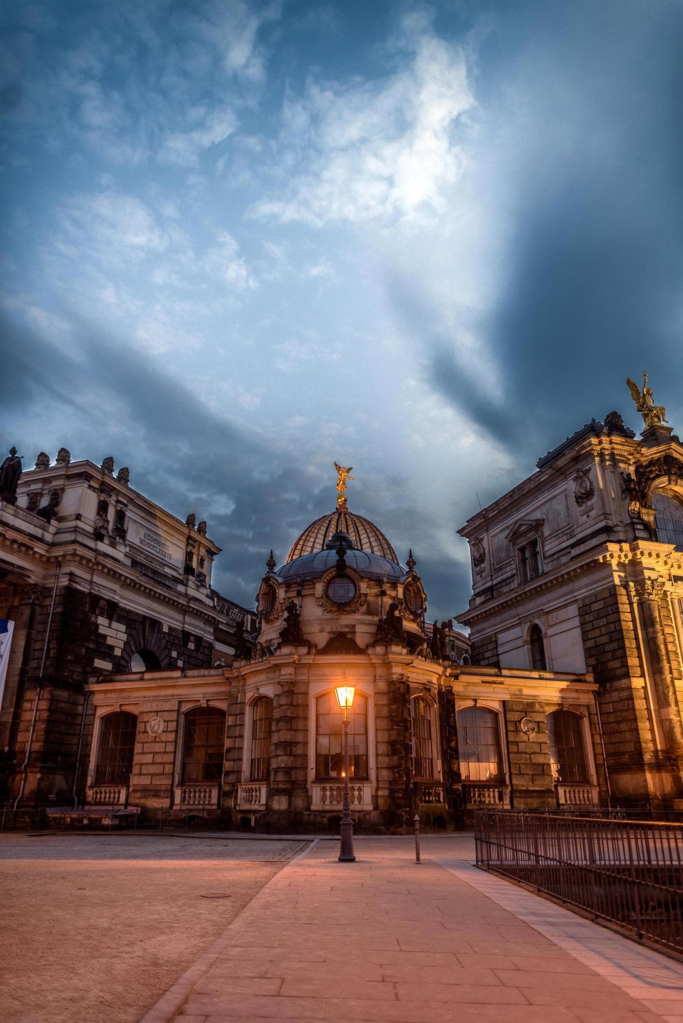 A building lit up at dusk in front of a cloudy sky.