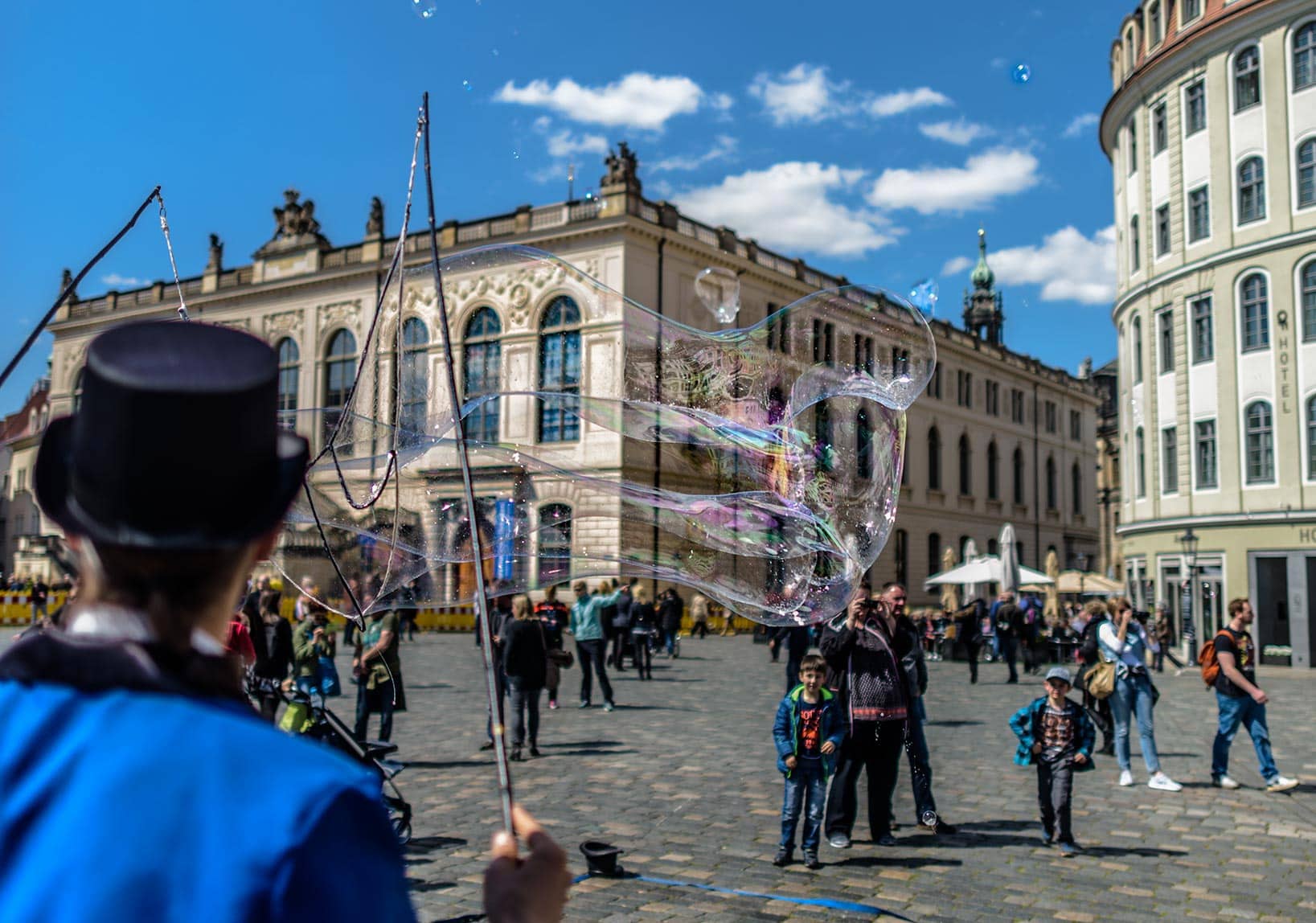 A man in a top hat is blowing bubbles in a square.