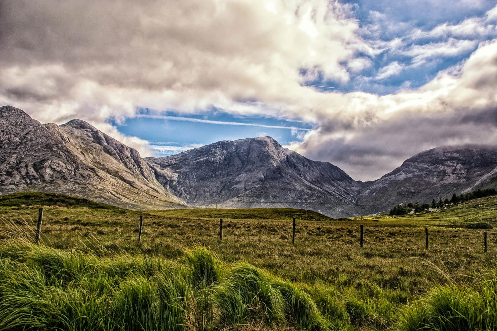 A field with grass and mountains under a cloudy sky.