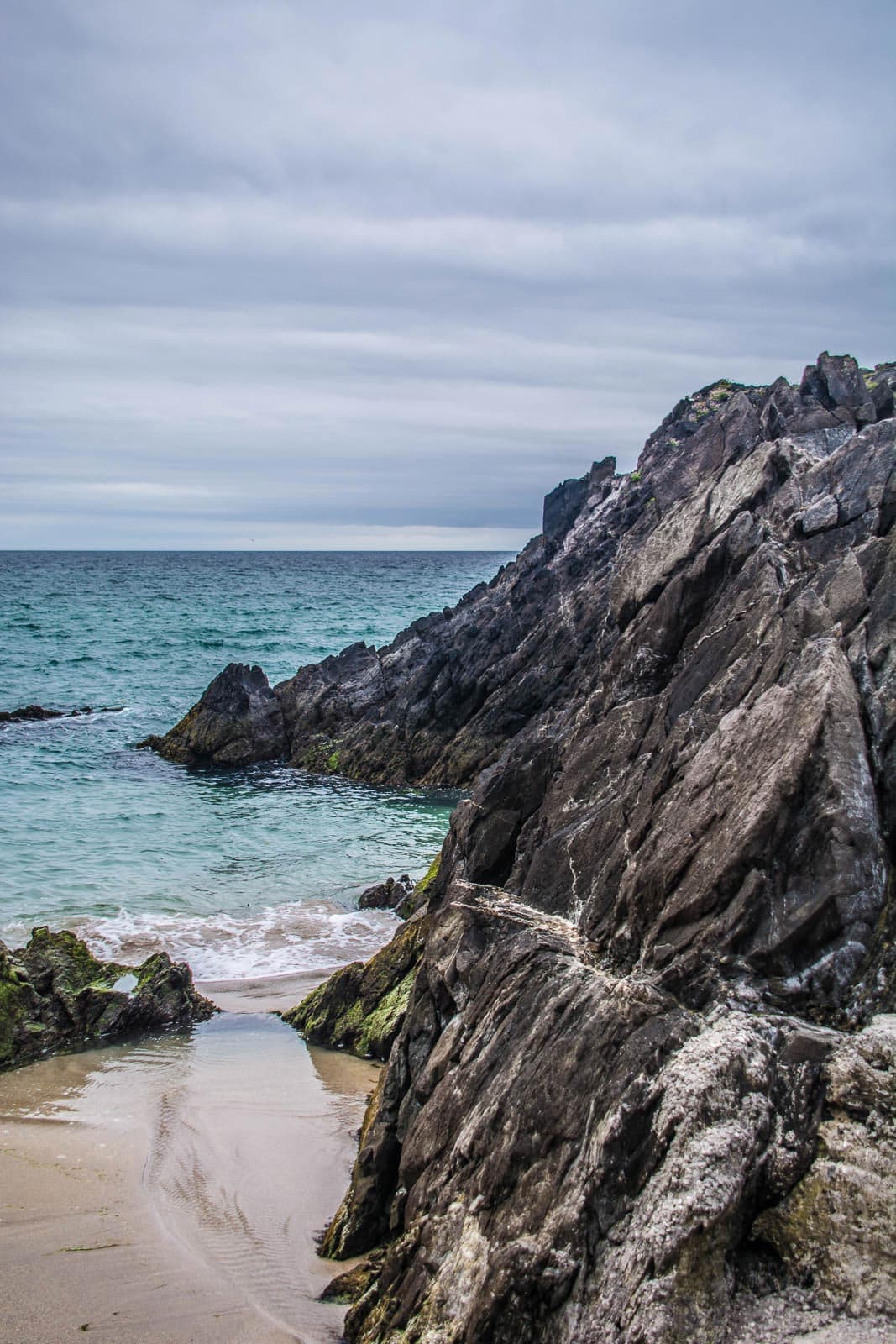 A rocky beach with water and a cloudy sky.