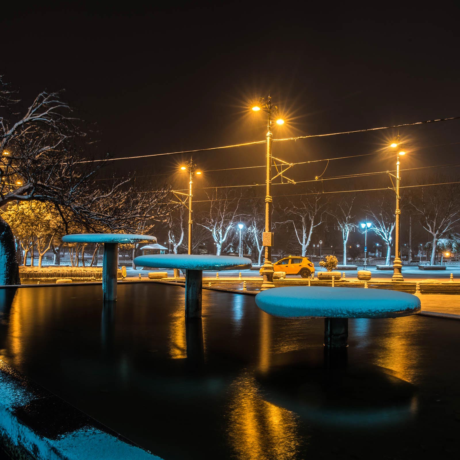 Snow covered benches in a park at night.