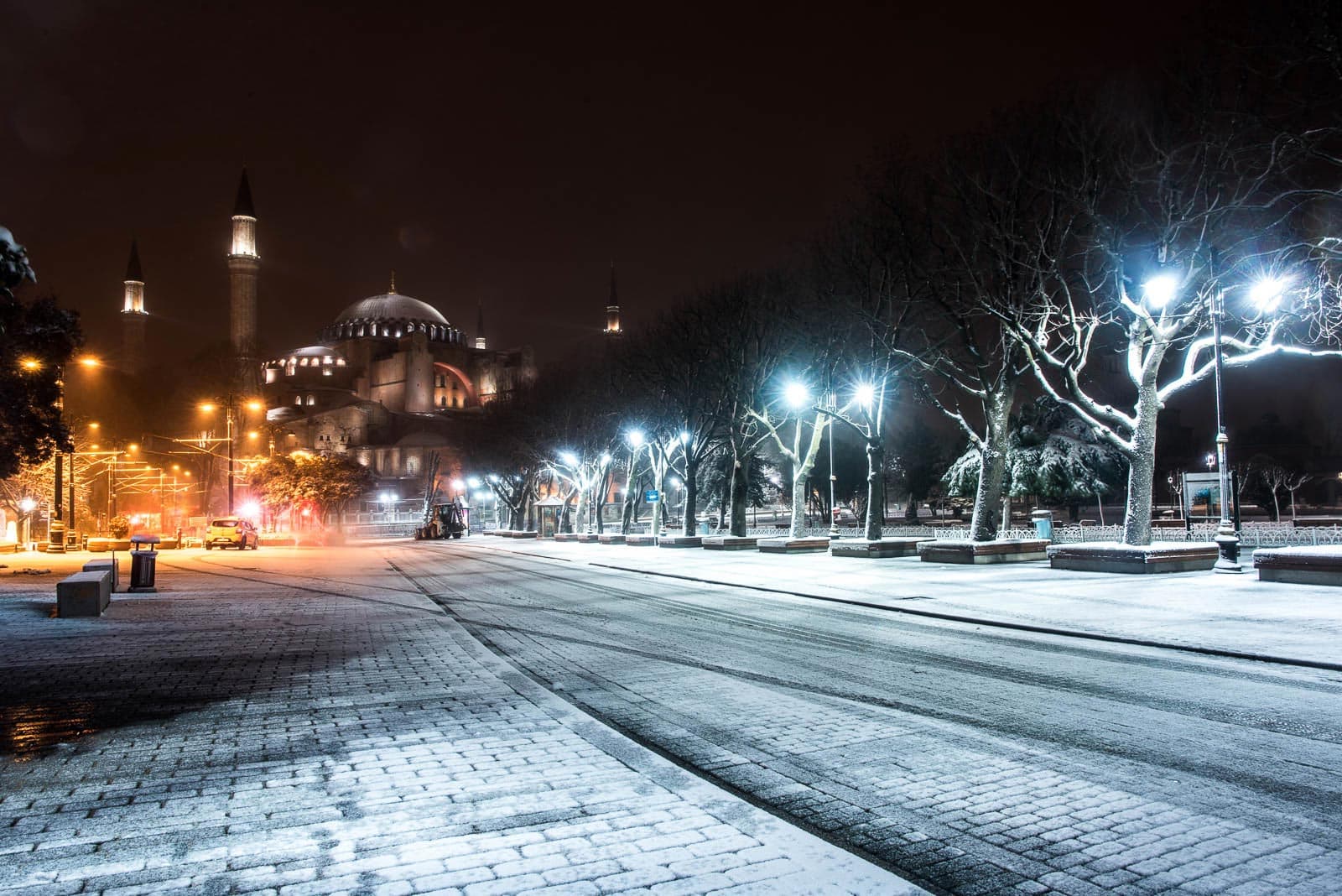 A snowy street with lights and a mosque in the background.