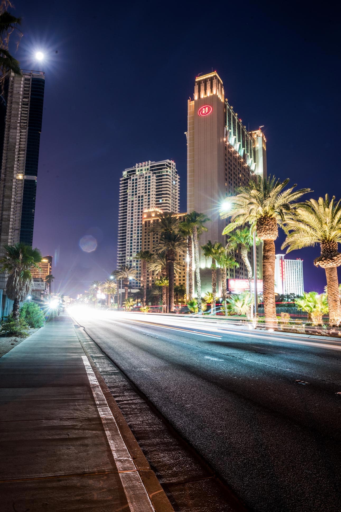 A street with palm trees and buildings at night.