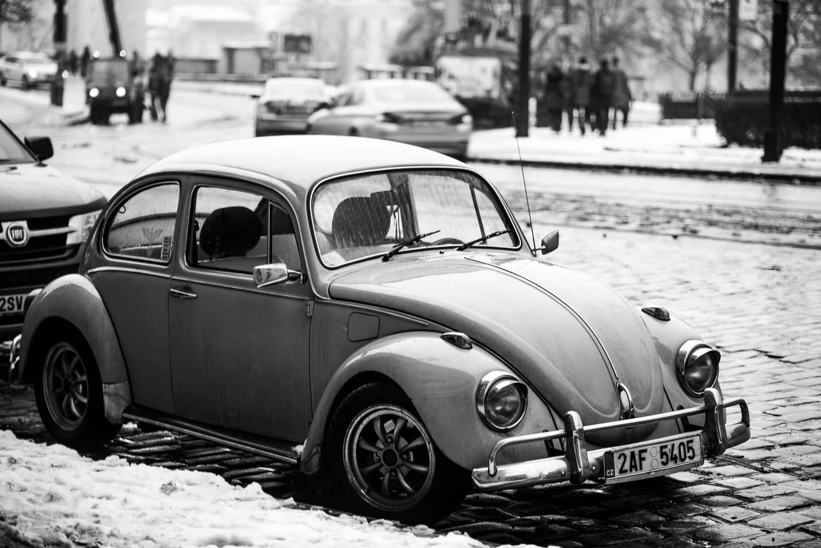 A black and white photo of a vw beetle parked on a snowy street.