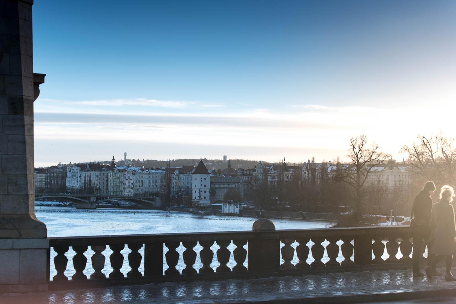 Two people standing on a bridge overlooking a city.