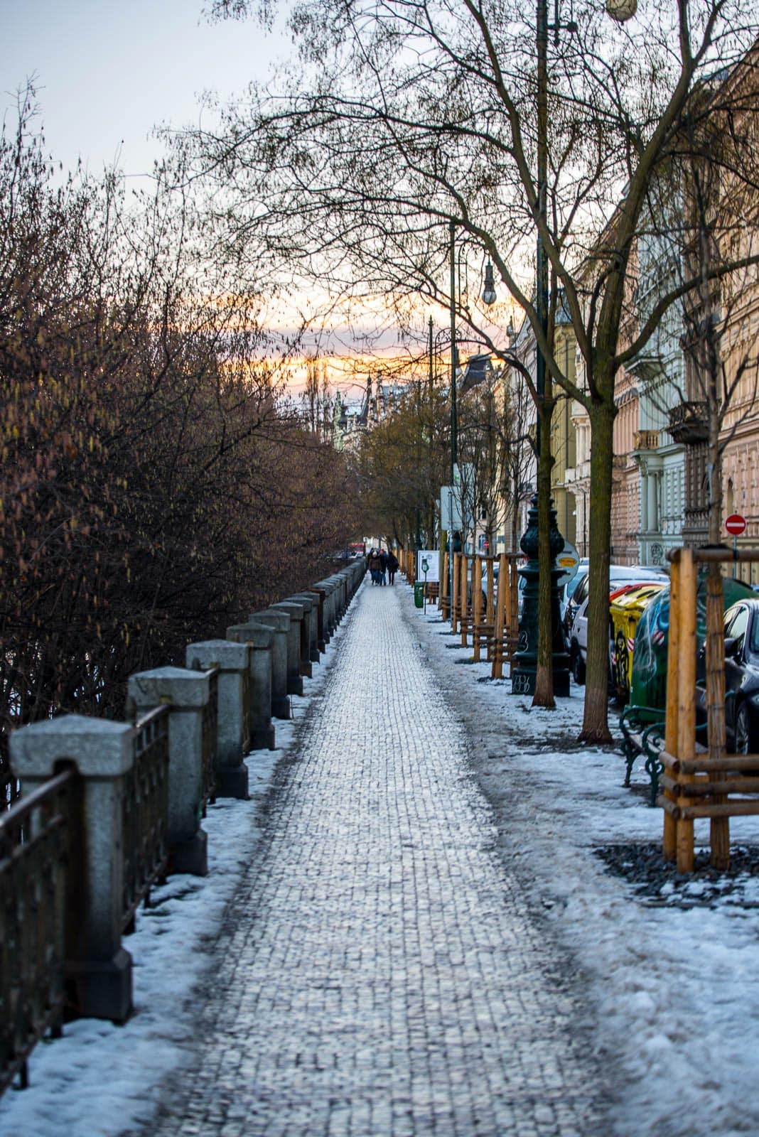 A sidewalk lined with snow and parked cars.