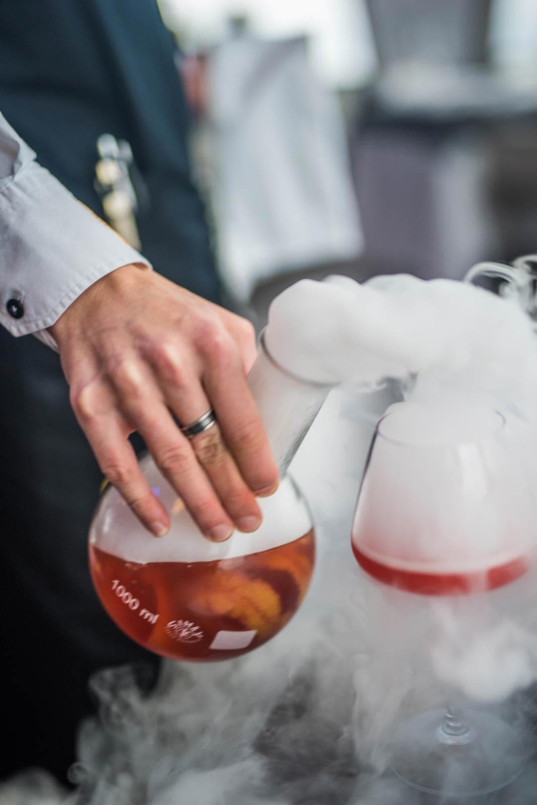 A bartender pouring a drink into a glass with smoke.