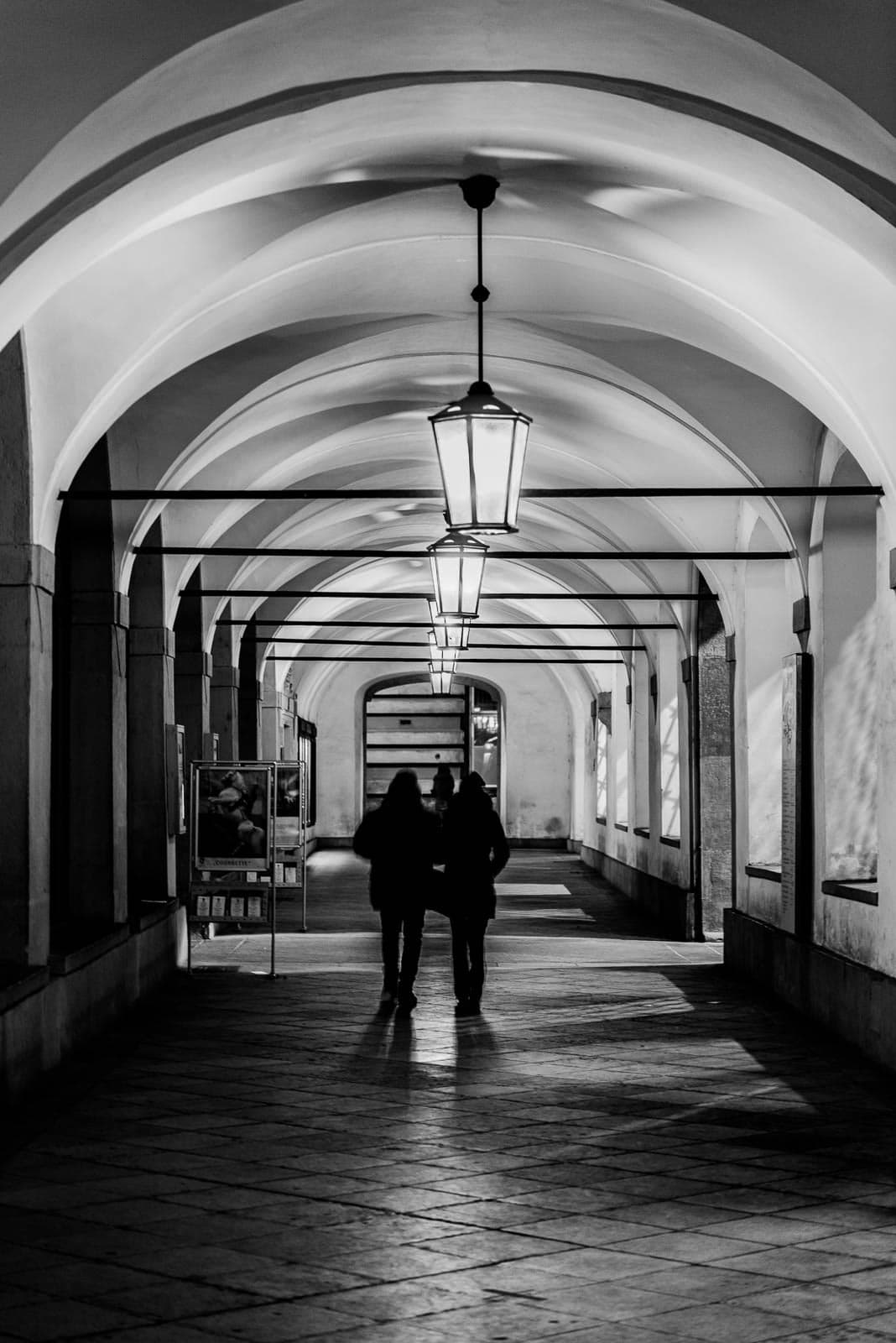 Two people walking under an archway in black and white.