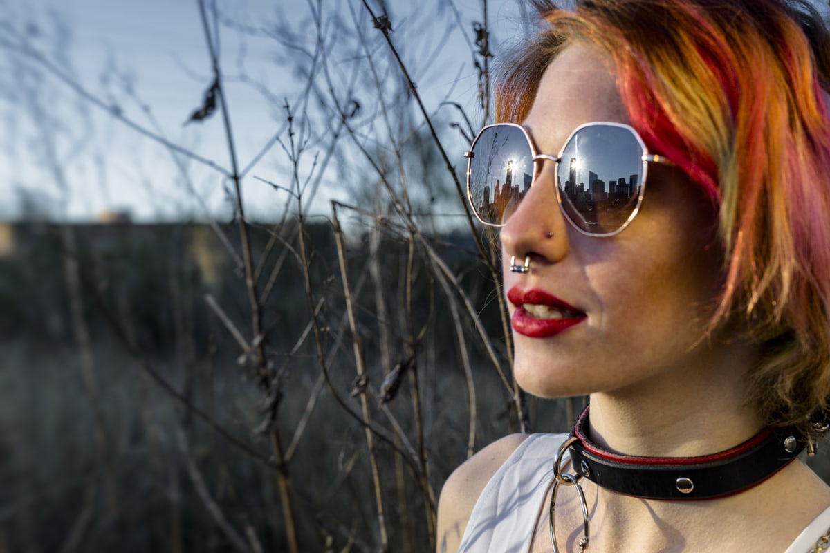 A woman with red hair wearing sunglasses and a choker.
