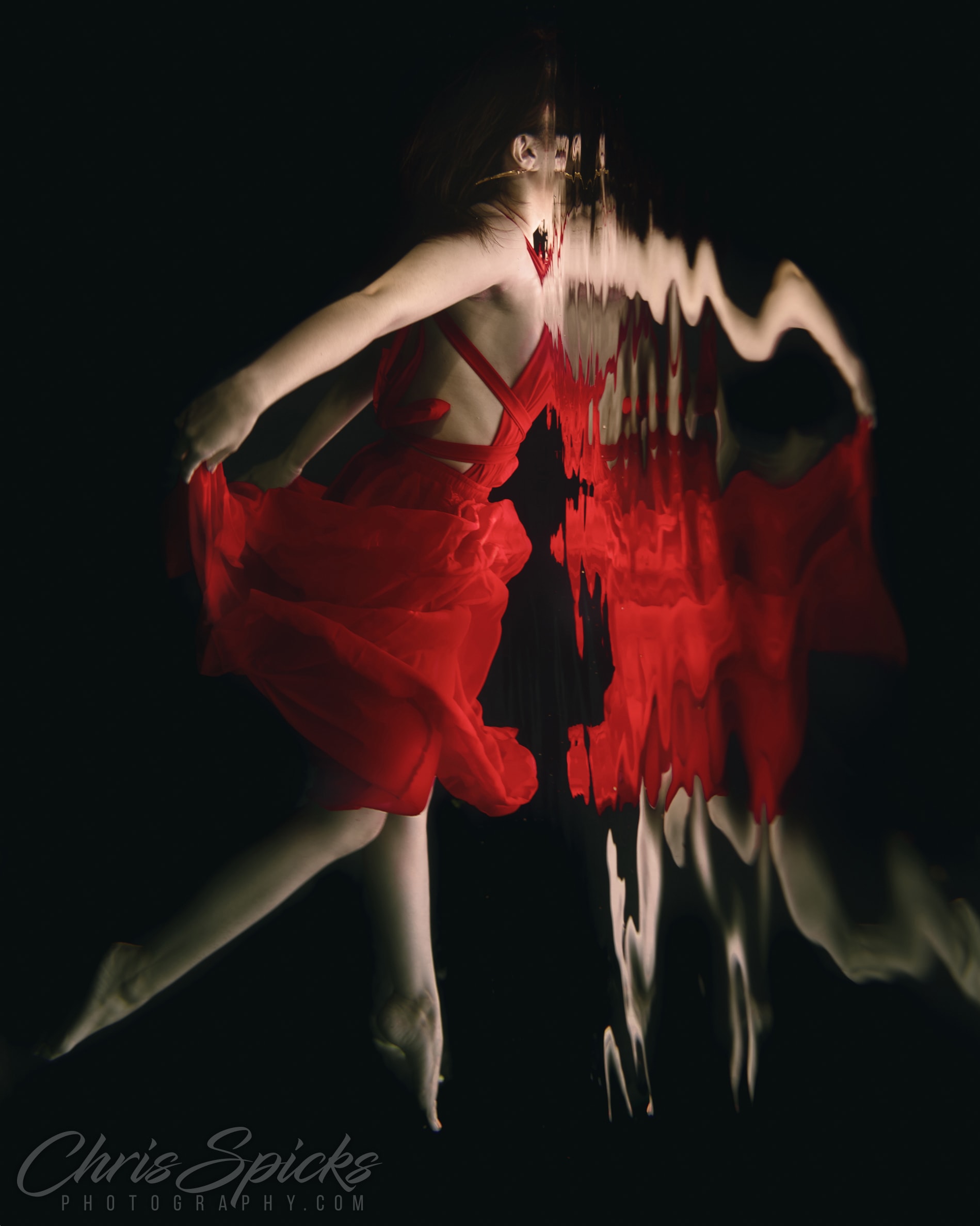 Houston Photographer Chris Spicks captures a mesmerizing moment of creative photography, showcasing a woman gracefully swimming underwater in a vibrant red dress.