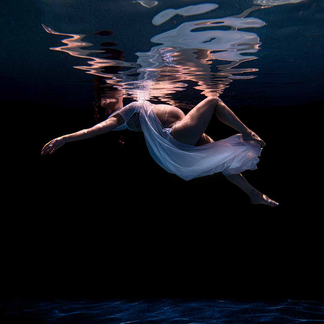 A woman in a white dress floating under water.