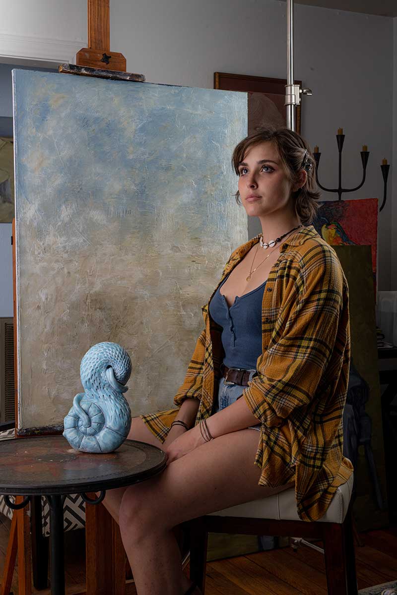 A woman sitting on a chair in front of an easel captured by Chris Spicks Photography, a creative Houston photographer.