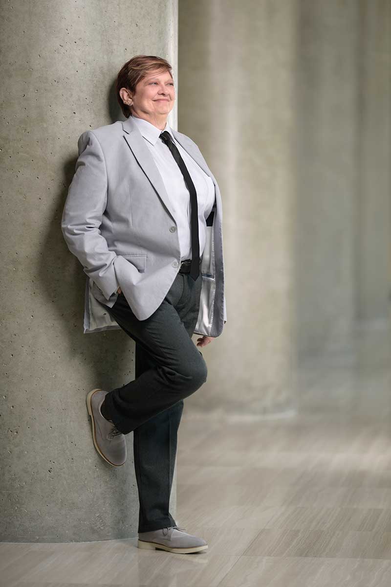 Chris Spicks Photography captures the creativity of a woman in a gray suit, effortlessly leaning against a column.