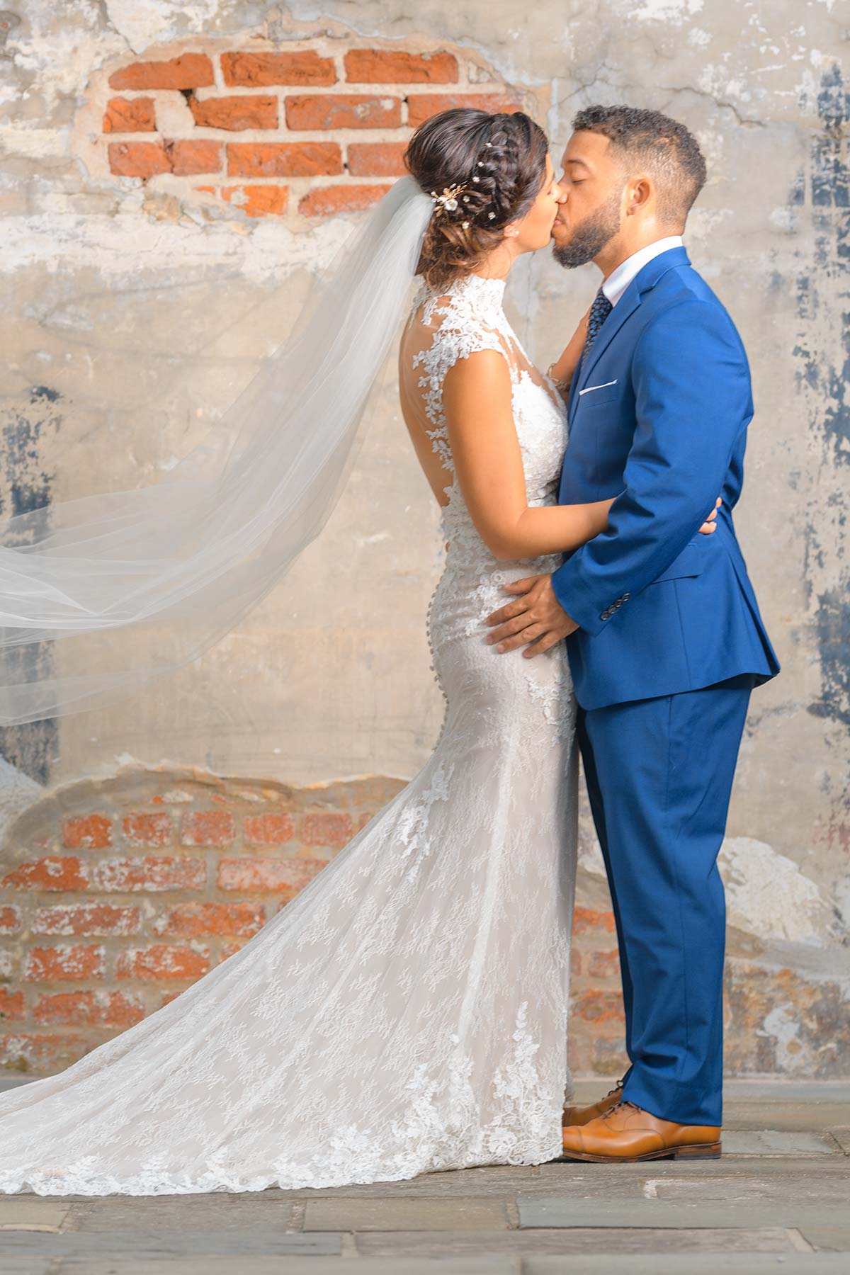 A bride and groom share a romantic kiss in front of an old brick wall captured by Chris Spicks Photography, Houston's creative photographer.