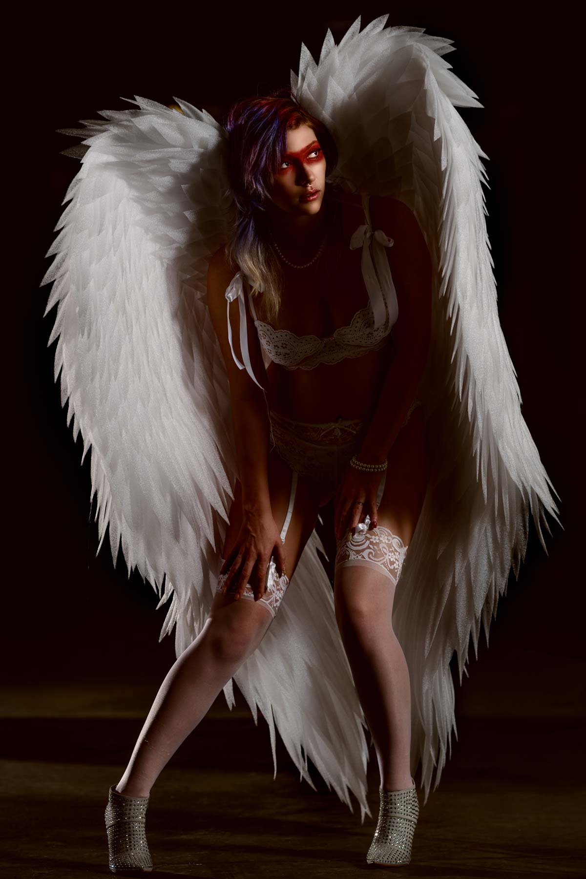 A woman with white wings posing in a dark room captured by Chris Spicks Photography, a creative Houston photographer.